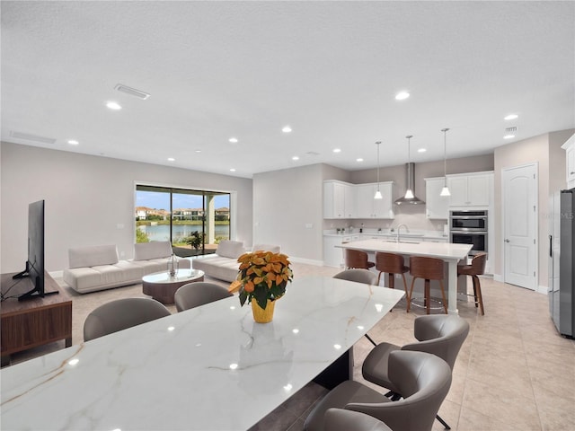 kitchen with sink, wall chimney exhaust hood, white cabinets, pendant lighting, and a water view