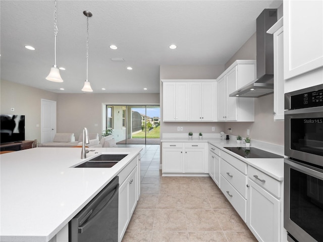 kitchen with wall chimney exhaust hood, a kitchen island with sink, sink, black appliances, and white cabinetry