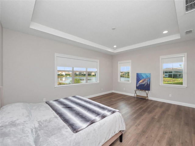 bedroom with a textured ceiling, a water view, dark wood-type flooring, and a tray ceiling