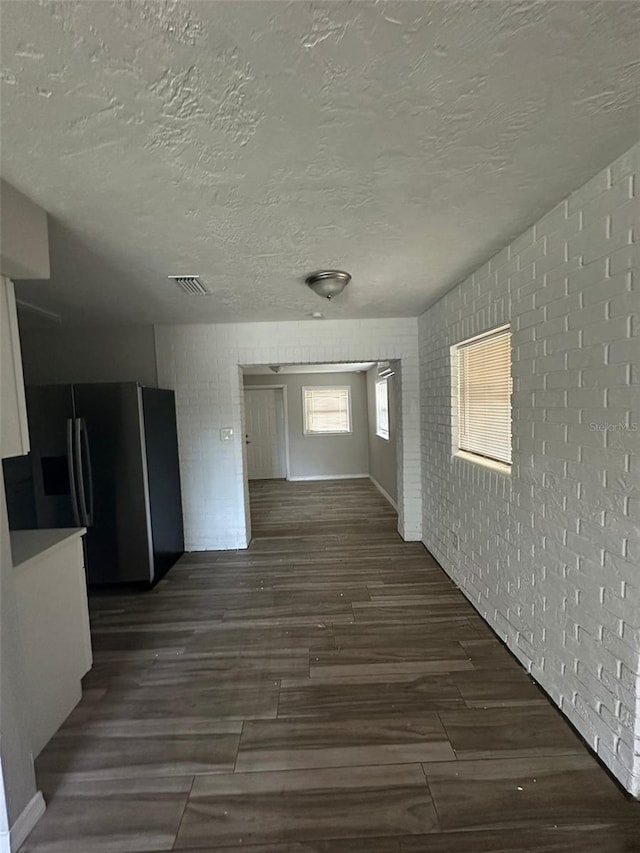 corridor with brick wall, dark wood-type flooring, and a textured ceiling