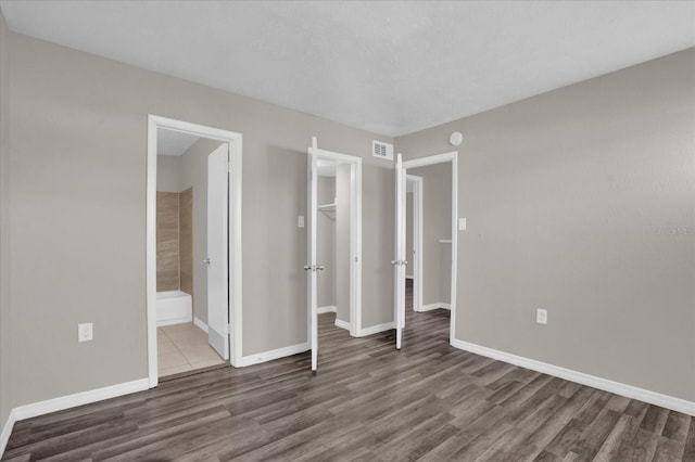 unfurnished bedroom with a walk in closet, ensuite bathroom, and dark hardwood / wood-style floors