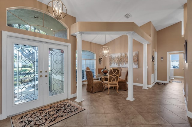 tiled entryway with decorative columns, french doors, and a chandelier