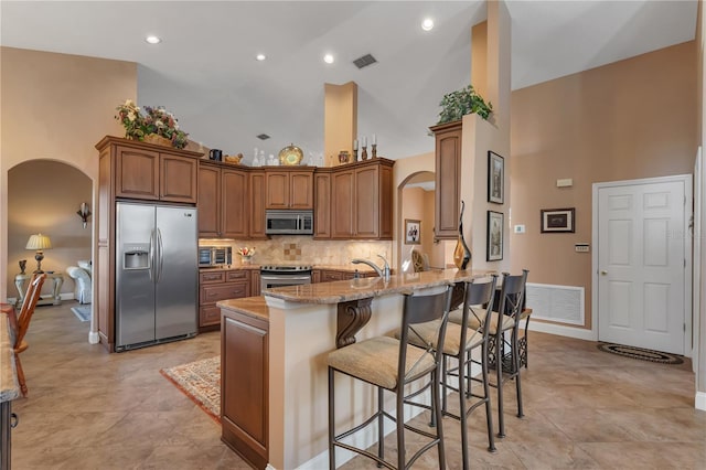 kitchen with kitchen peninsula, light stone counters, a breakfast bar, stainless steel appliances, and high vaulted ceiling