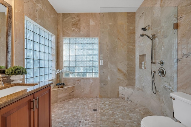 bathroom featuring a tile shower, vanity, toilet, and a wealth of natural light