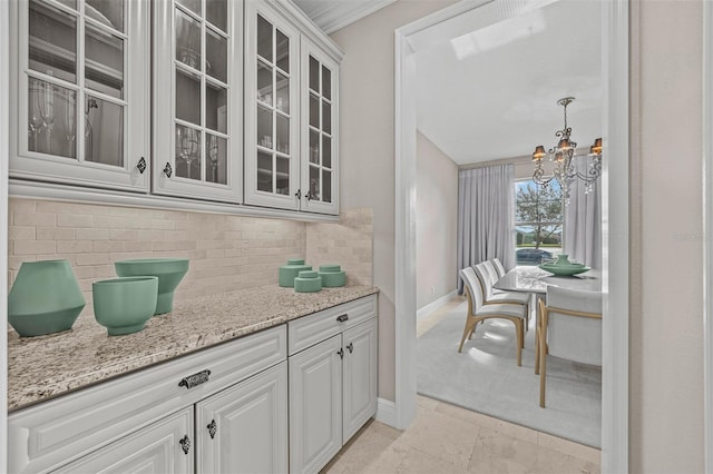 kitchen featuring light stone countertops, a notable chandelier, decorative light fixtures, white cabinets, and ornamental molding