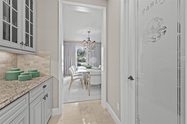 interior space with white cabinetry, light stone counters, a chandelier, pendant lighting, and decorative backsplash