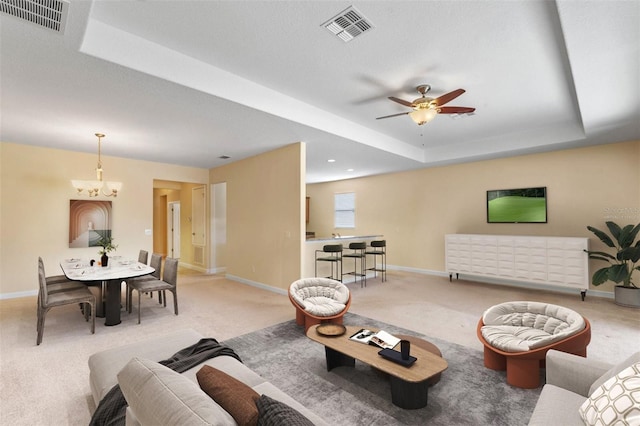 carpeted living room with a textured ceiling, ceiling fan with notable chandelier, and a raised ceiling