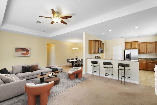 carpeted living room featuring ceiling fan with notable chandelier and a raised ceiling