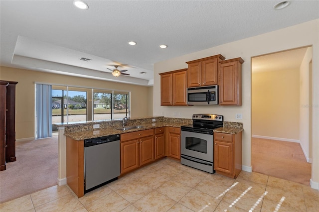 kitchen featuring kitchen peninsula, light carpet, appliances with stainless steel finishes, and dark stone counters