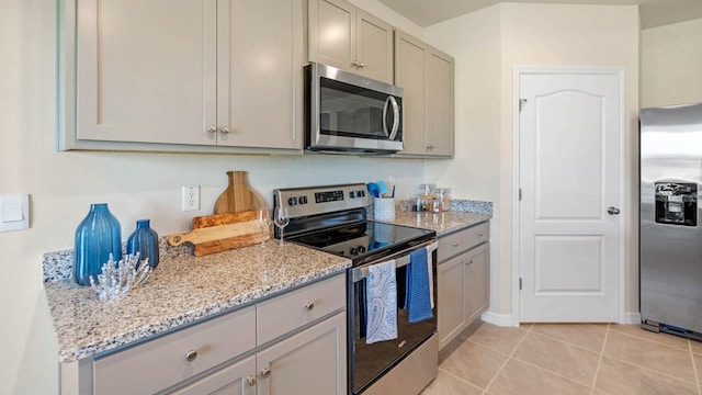 kitchen with gray cabinets, light stone countertops, light tile patterned floors, and stainless steel appliances