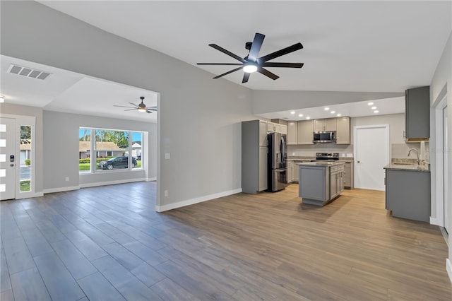 kitchen featuring lofted ceiling, gray cabinets, light wood-type flooring, a kitchen island, and stainless steel appliances