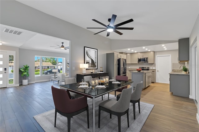 dining area with ceiling fan, light wood-type flooring, sink, and vaulted ceiling