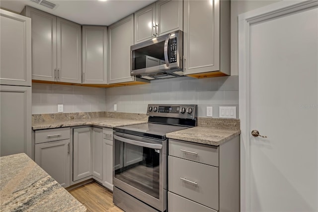 kitchen featuring light stone countertops, appliances with stainless steel finishes, light wood-type flooring, backsplash, and gray cabinets