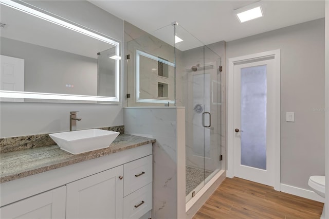 bathroom with hardwood / wood-style floors, vanity, toilet, and a shower with shower door