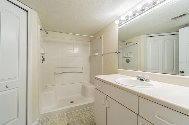 bathroom featuring vanity, a tile shower, and a textured ceiling