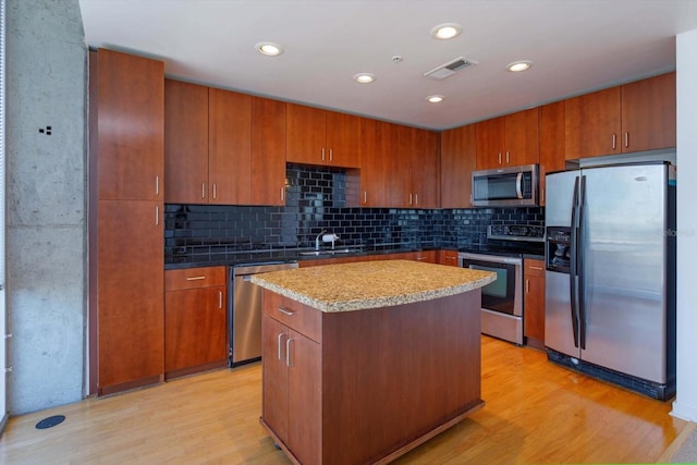 kitchen featuring a kitchen island, light wood-type flooring, appliances with stainless steel finishes, and tasteful backsplash