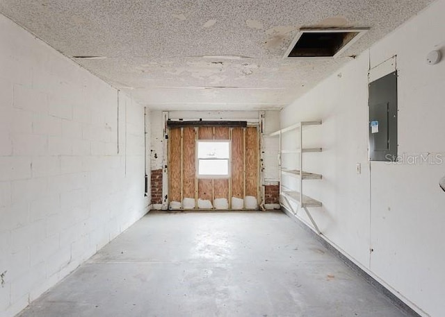 empty room with concrete block wall, electric panel, and unfinished concrete floors