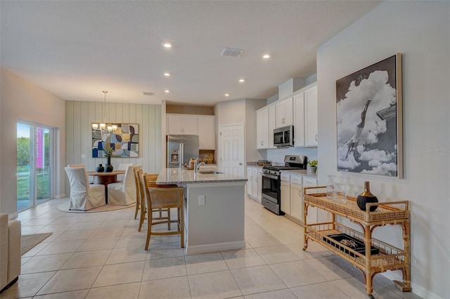 kitchen featuring pendant lighting, a kitchen island with sink, light stone countertops, appliances with stainless steel finishes, and white cabinetry