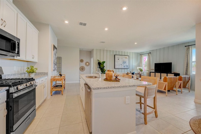 kitchen with white cabinetry, an island with sink, light stone countertops, and appliances with stainless steel finishes