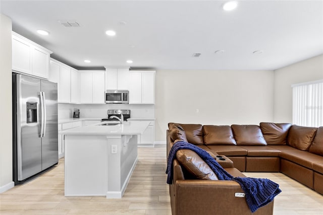 kitchen featuring white cabinets, light wood-type flooring, an island with sink, and appliances with stainless steel finishes