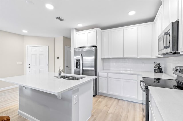 kitchen with sink, tasteful backsplash, light hardwood / wood-style flooring, a center island with sink, and appliances with stainless steel finishes