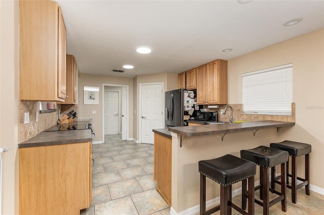 kitchen featuring sink, stainless steel fridge with ice dispenser, backsplash, kitchen peninsula, and a kitchen bar