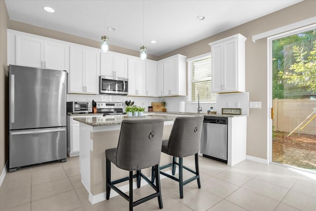 kitchen featuring a center island, white cabinets, a kitchen breakfast bar, light stone countertops, and appliances with stainless steel finishes