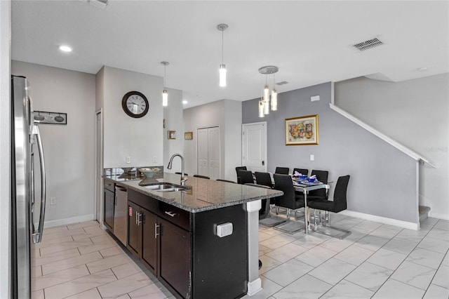 kitchen with dark brown cabinetry, sink, hanging light fixtures, dark stone countertops, and appliances with stainless steel finishes