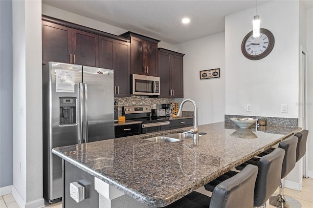 kitchen with dark stone countertops, a sink, dark brown cabinetry, a peninsula, and appliances with stainless steel finishes