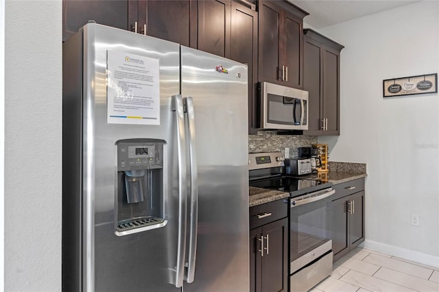 kitchen with stainless steel appliances, dark stone countertops, tasteful backsplash, dark brown cabinets, and baseboards