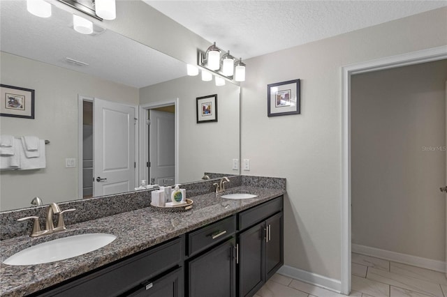 full bathroom with baseboards, a sink, a textured ceiling, and double vanity