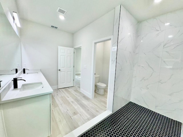 bathroom with tiled shower, vanity, wood-type flooring, and toilet