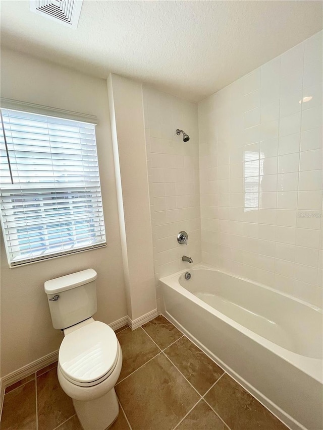 bathroom featuring toilet, a textured ceiling, tiled shower / bath combo, and tile patterned floors