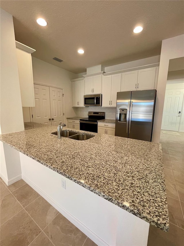 kitchen featuring white cabinets, sink, light stone counters, kitchen peninsula, and stainless steel appliances