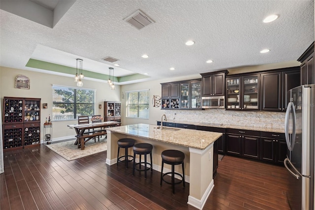 kitchen with dark wood-type flooring, sink, hanging light fixtures, an island with sink, and stainless steel appliances