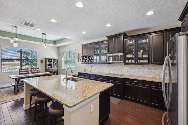 kitchen featuring appliances with stainless steel finishes, a kitchen island with sink, sink, dark hardwood / wood-style floors, and hanging light fixtures