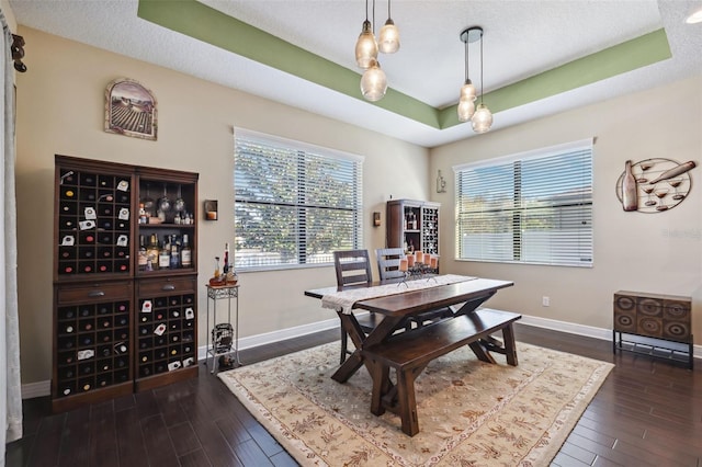 dining room with a textured ceiling, dark hardwood / wood-style flooring, and a tray ceiling