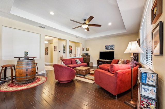 living room with dark hardwood / wood-style floors, a raised ceiling, and ceiling fan