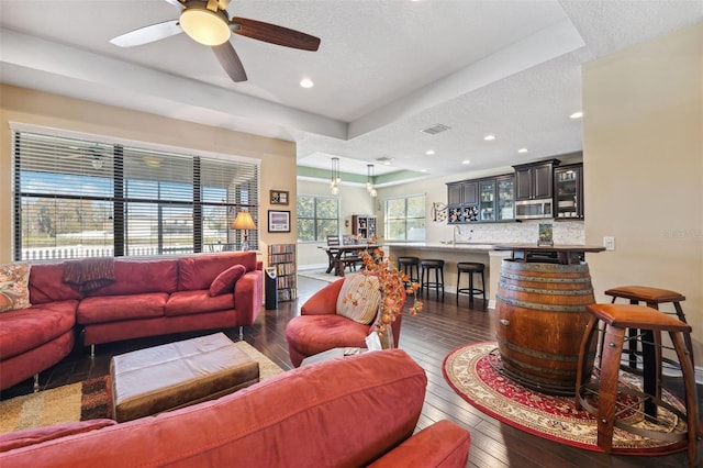 living room featuring a textured ceiling, dark hardwood / wood-style flooring, a tray ceiling, and ceiling fan