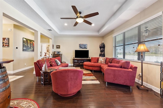 living room featuring a tray ceiling, ceiling fan, and dark wood-type flooring