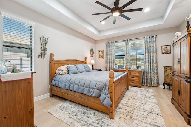 bedroom featuring a raised ceiling, ceiling fan, and light wood-type flooring