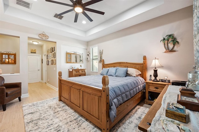 bedroom with a tray ceiling, ceiling fan, and light hardwood / wood-style flooring