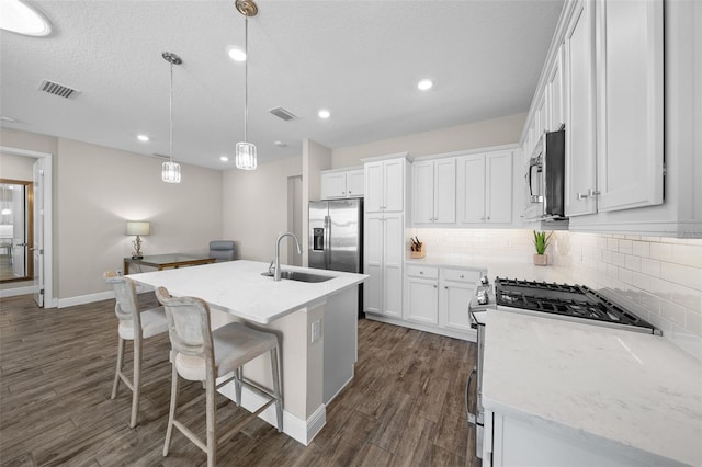 kitchen featuring dark hardwood / wood-style floors, decorative light fixtures, a kitchen island with sink, white cabinets, and appliances with stainless steel finishes