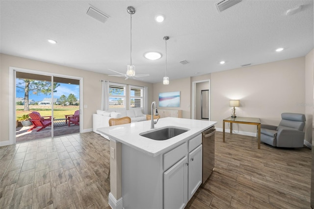 kitchen featuring sink, hanging light fixtures, stainless steel dishwasher, an island with sink, and light hardwood / wood-style floors