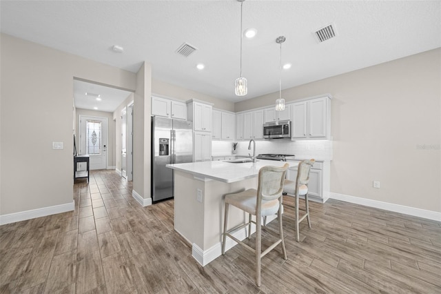 kitchen featuring white cabinetry, light hardwood / wood-style flooring, a breakfast bar area, a center island with sink, and appliances with stainless steel finishes