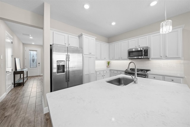 kitchen featuring white cabinetry, light stone counters, pendant lighting, wood-type flooring, and appliances with stainless steel finishes