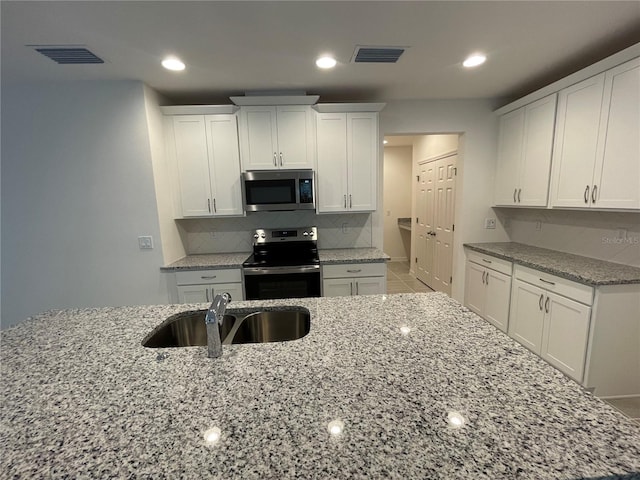 kitchen featuring appliances with stainless steel finishes, light stone counters, white cabinetry, and sink