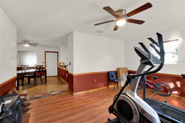 workout room featuring a textured ceiling, light wood-type flooring, and ceiling fan