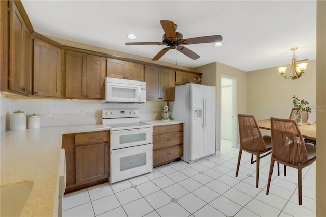 kitchen with backsplash, ceiling fan with notable chandelier, white appliances, pendant lighting, and light tile patterned floors