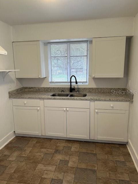 kitchen featuring white cabinetry, sink, and light stone countertops